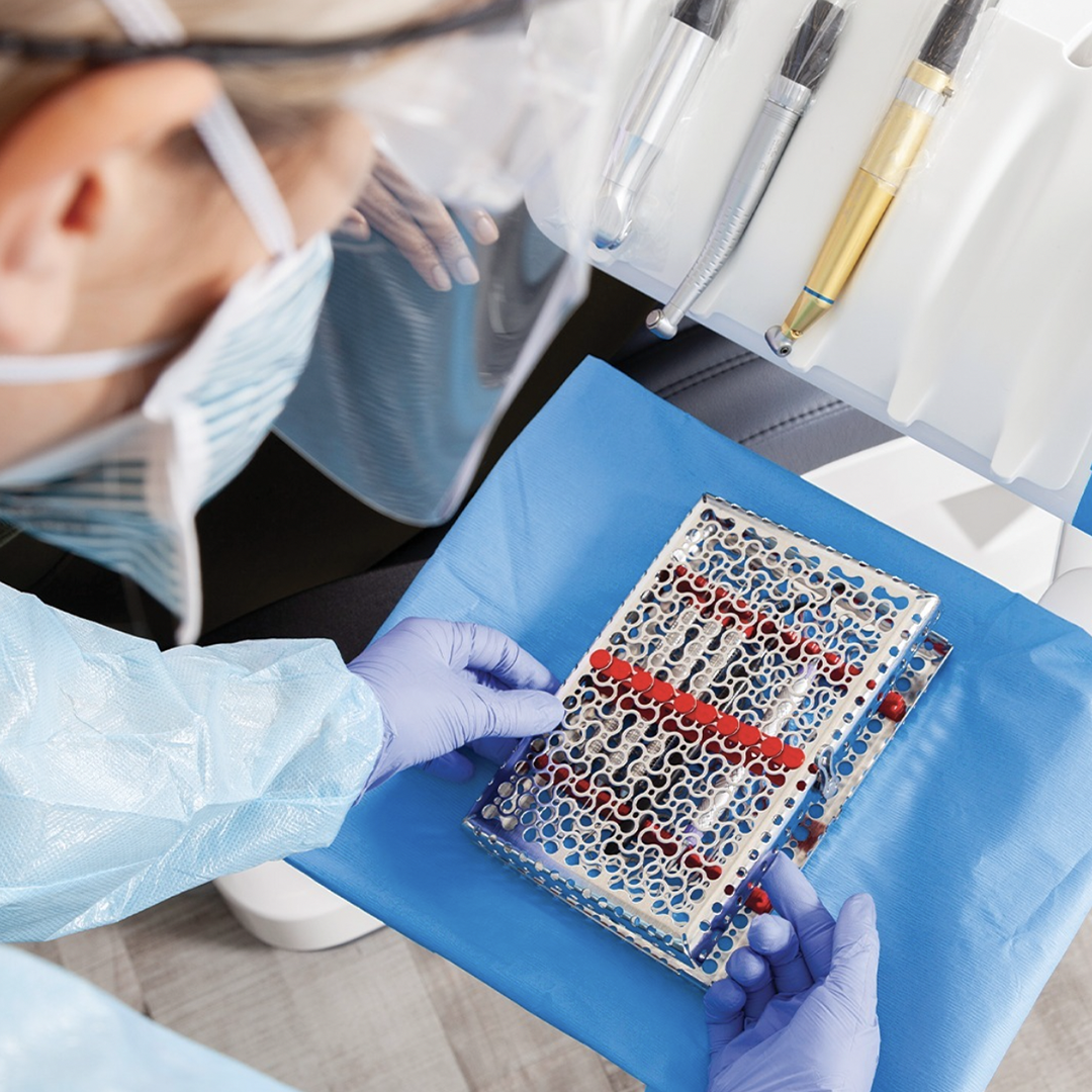 Dental clinician wearing gloves and protective equipment handling an IMS cassette on a blue drape